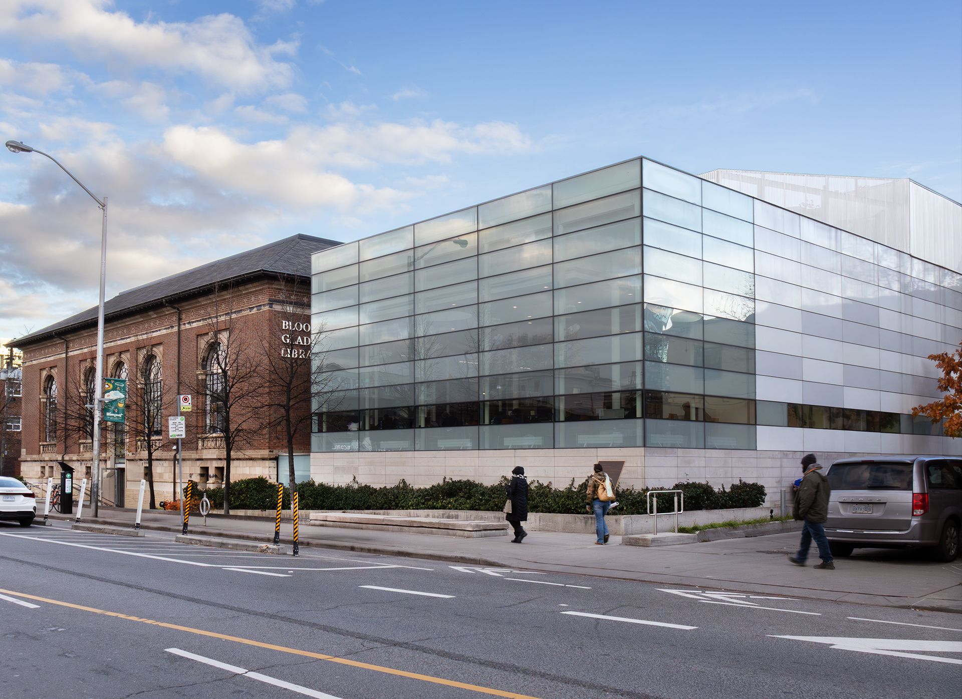 A red and cream brick building, with a gray roof, and a glass building extension, across a street. An accessibility ramp leads to the entrance of the red and cream brick building.