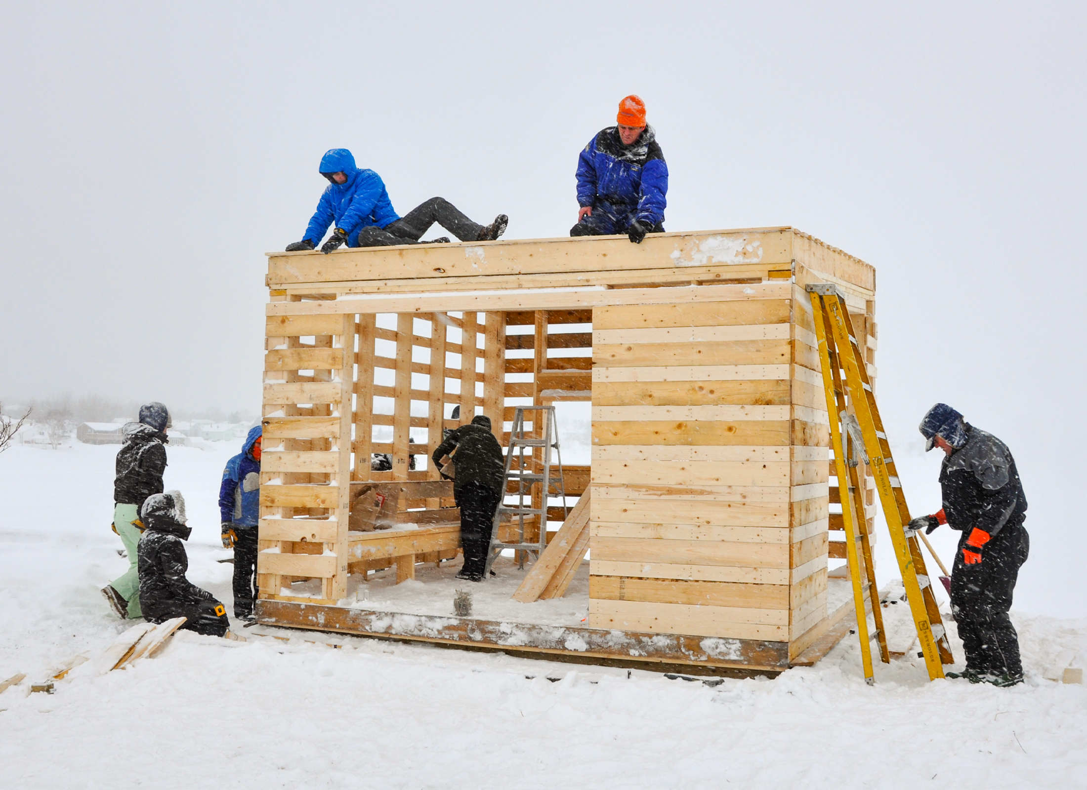 People building a wooden structure sitting on a snowy northern lake.