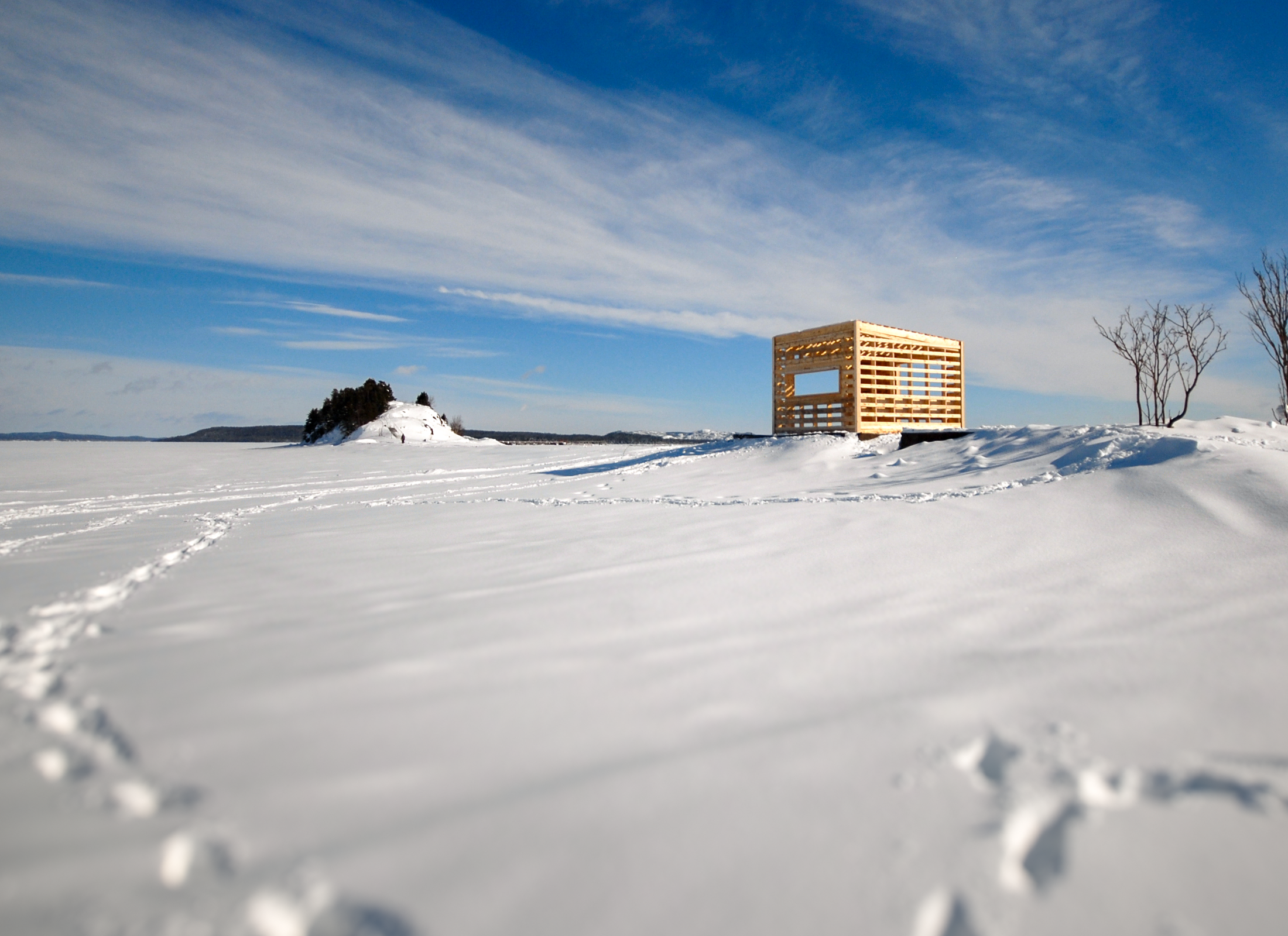 Wooden structure sitting on a mound of snow on a northern lake.