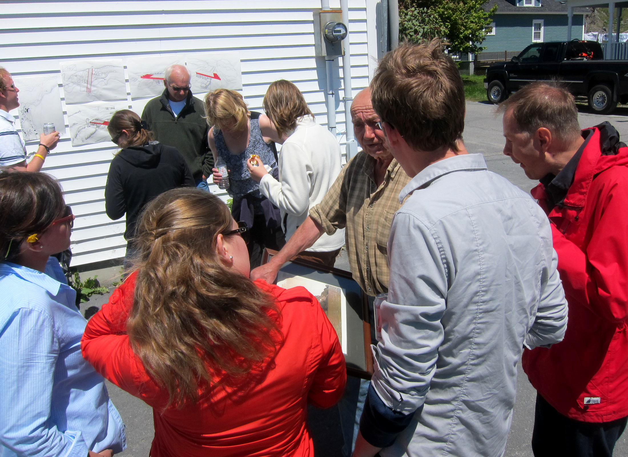 Group of people standing outside looking at pieces of paper.