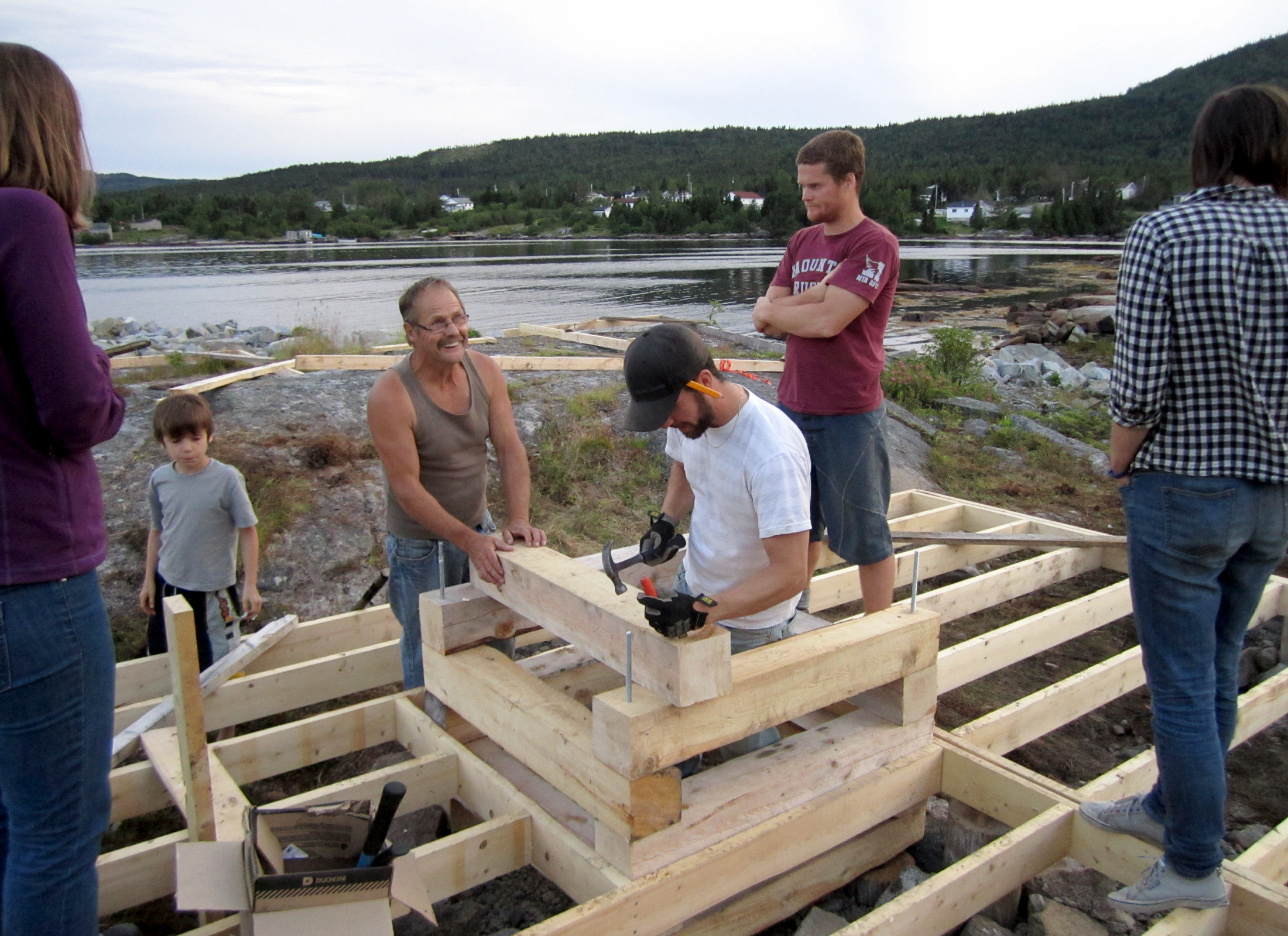 People building a timber structure by the waterfront.