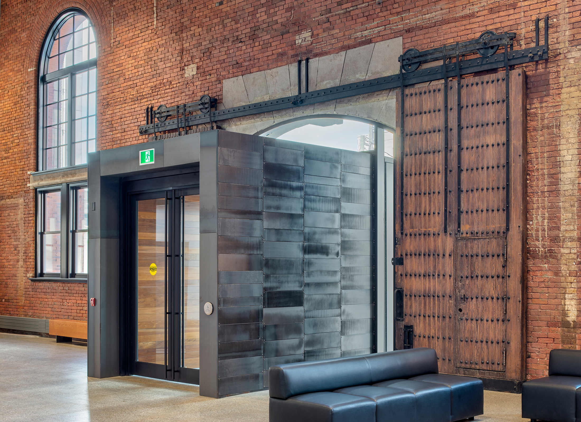 Entryway of the Windsor Armouries, a modern entryway with historical doors, a brick wall and glass arched windows