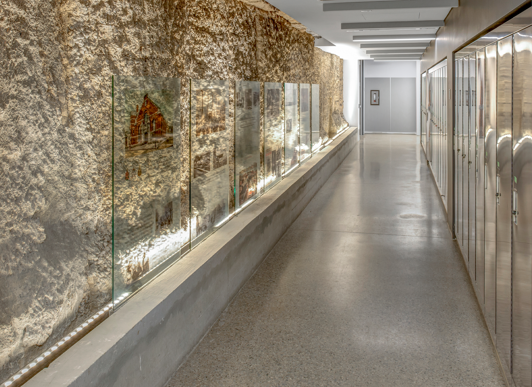 Hallway inside Windsor Armory with a stone wall on the left, images with the history of the building, and lockers on the right.