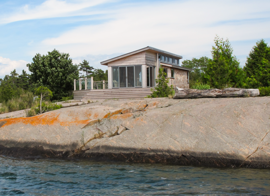 a bunkie with a slanted roof and glass sliding doors with a patio overlooking the lake.