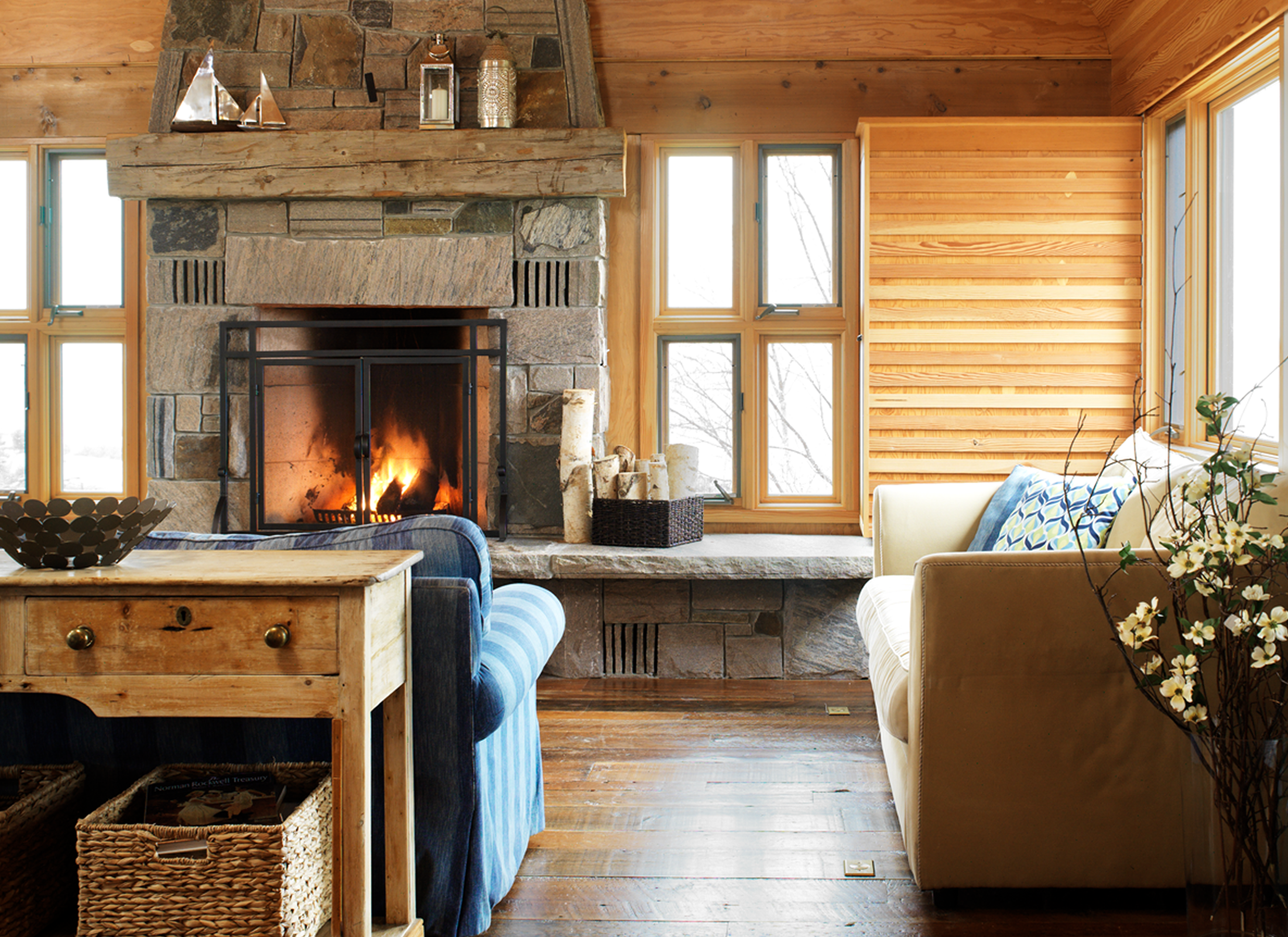 Living room with wooden walls, ceilings and floors. The room also holds a large stone fireplace.