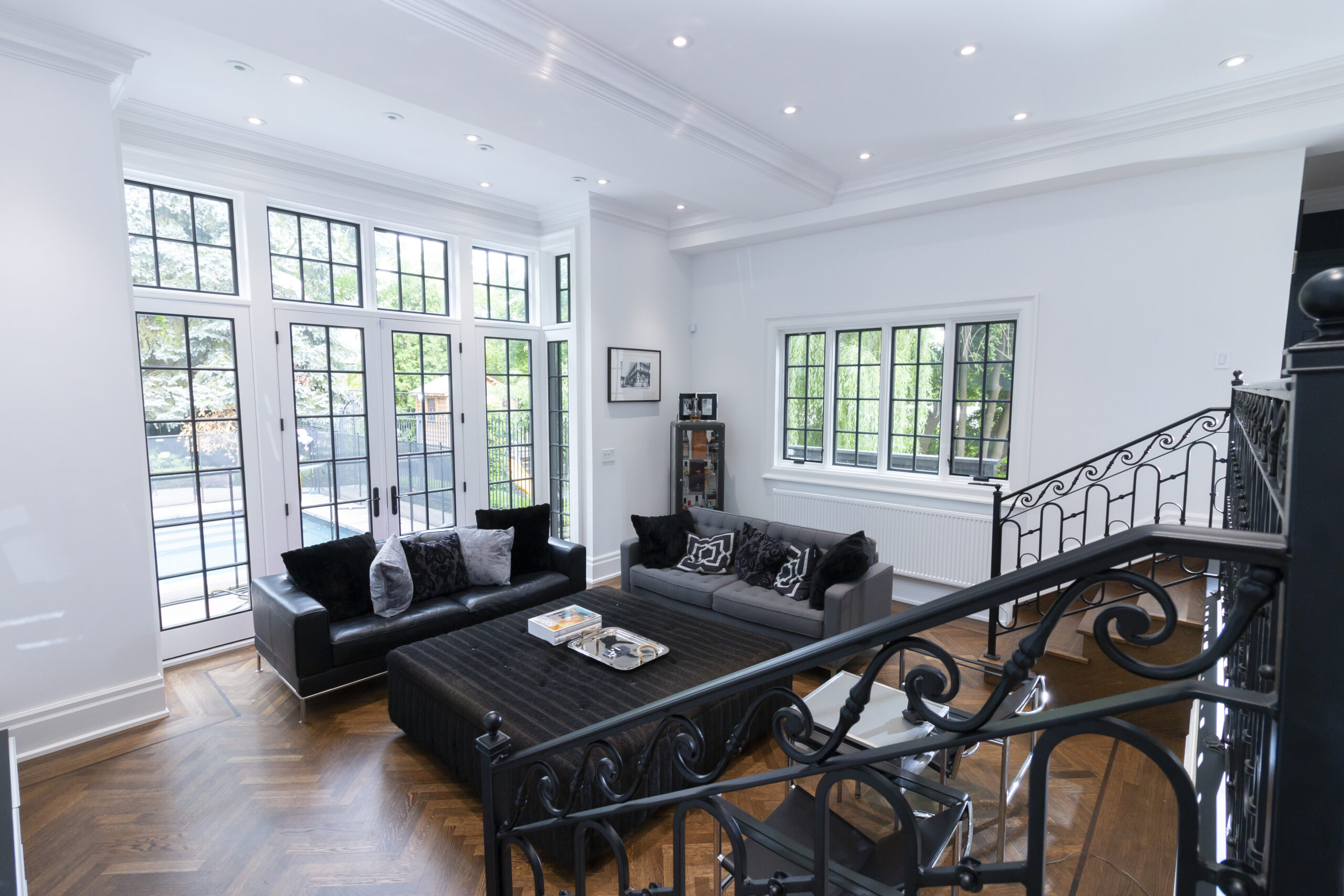 photo showing a living room area with two black couches and a large black coffee table. behind it is a wall of windows and a glazed doorway