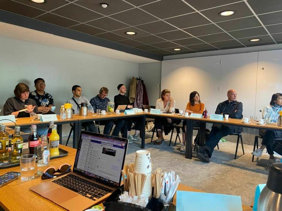 meeting with nine people sitting around a table watching a presentation