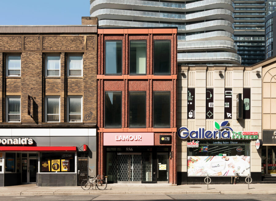 Elevation of 556 Yonge Street, a three storey building with large single pane windows, red brick, and ground floor retail.