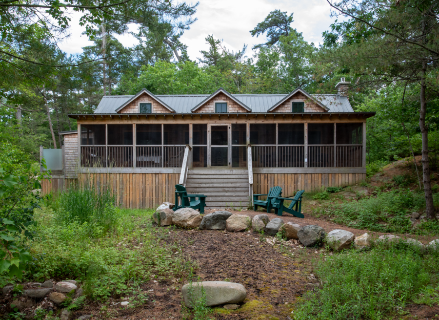 Exterior front view of Ballentine Pinewood cottage with cedar siding, black tin roof, large patio, three dormer windows, settled into a lush green forest.