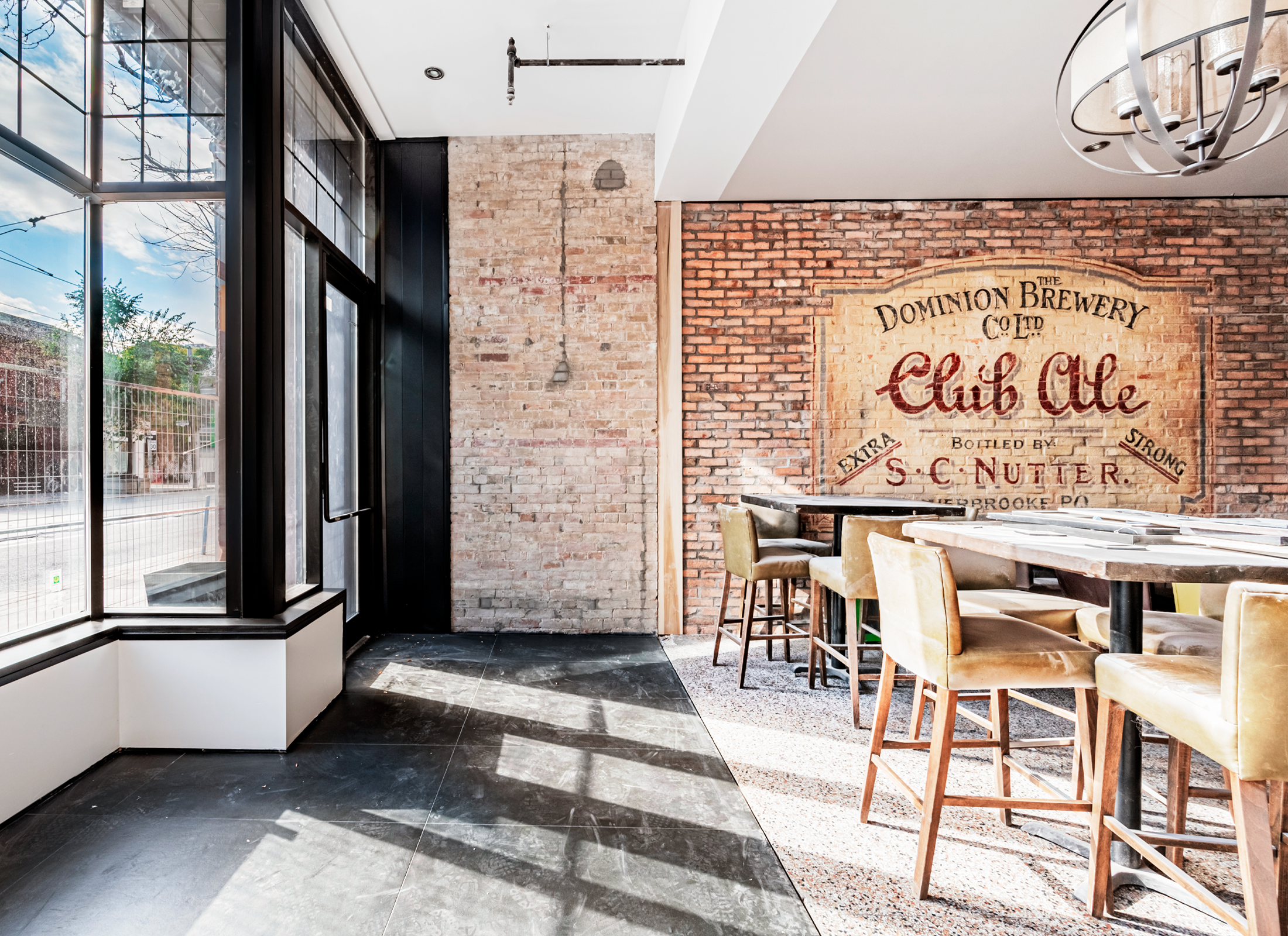 Inside a restaurant with a brick wall, tall glass windows, and high top seating.