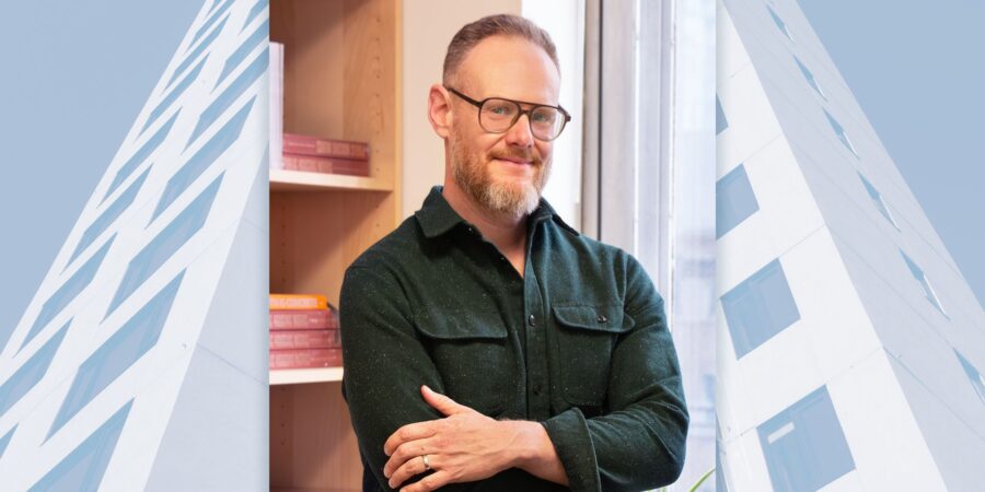 Graeme Stewart standing with his arms crossed in front of a book case and window.