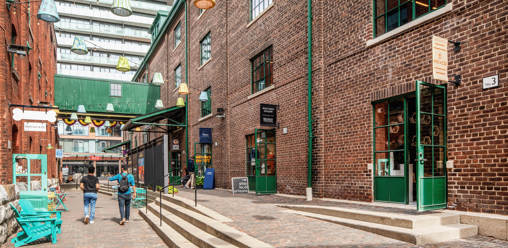 Pedestrian laneway framed by the Case Goods and Cannery buildings with green-trimmed storefronts.